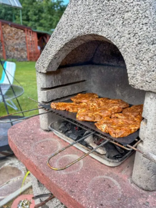Murowany grill z rusztem pełnym mięsa, w tle wiaty