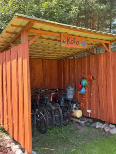 Rowery pod drewnianą wiatą z malowanym szyldem, w słońcu